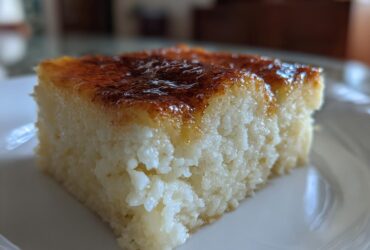 A close-up, side view of a square slice of moist cassava cake with a rich, caramelized brown topping.