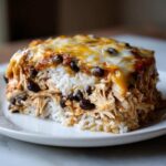 Close-up of a layered slice of burrito bake featuring shredded chicken, white rice, black beans, and melted cheese topping.