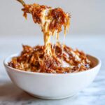 A spoonful of hot, cheesy caramelized onion dip showing a dramatic cheese pull over a white bowl.