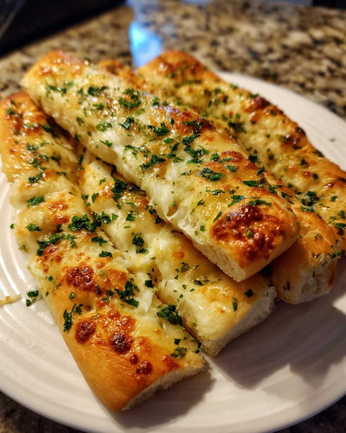 Close-up of four cheesy garlic breadsticks topped with melted cheese and fresh green parsley.