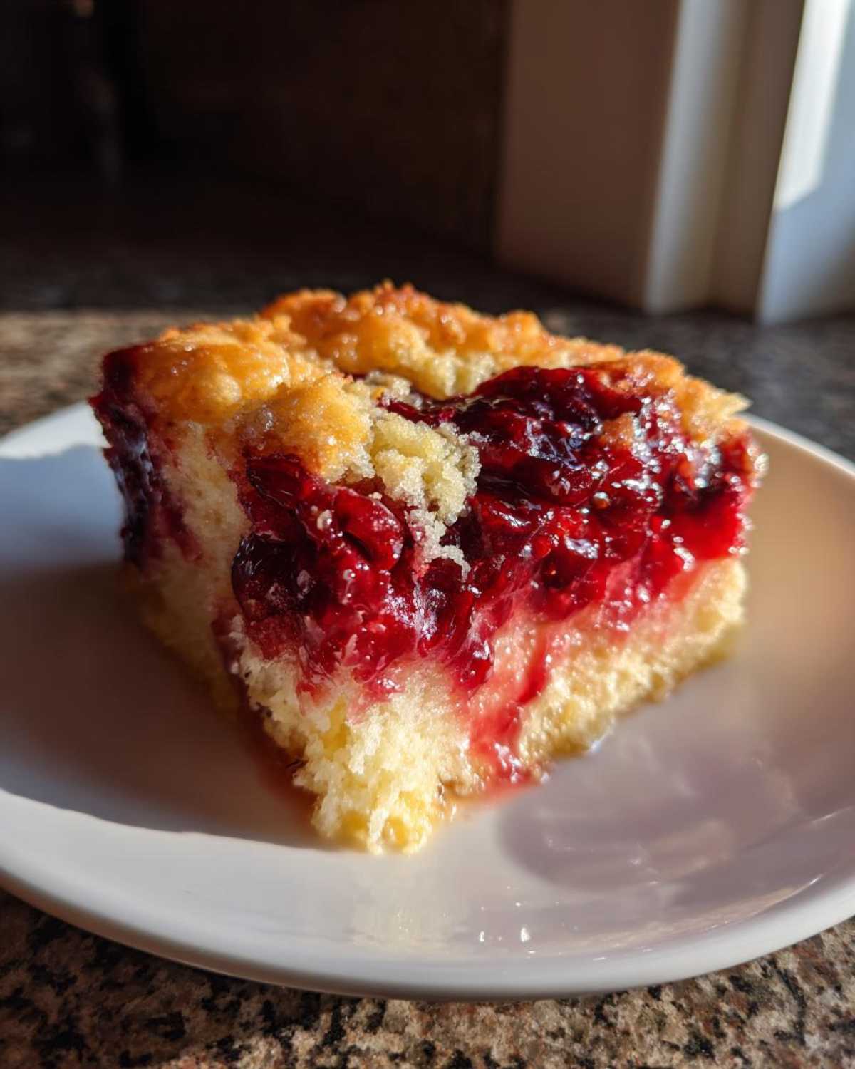 A square slice of bright red cherry dump cake with a crumbly topping served on a white plate.