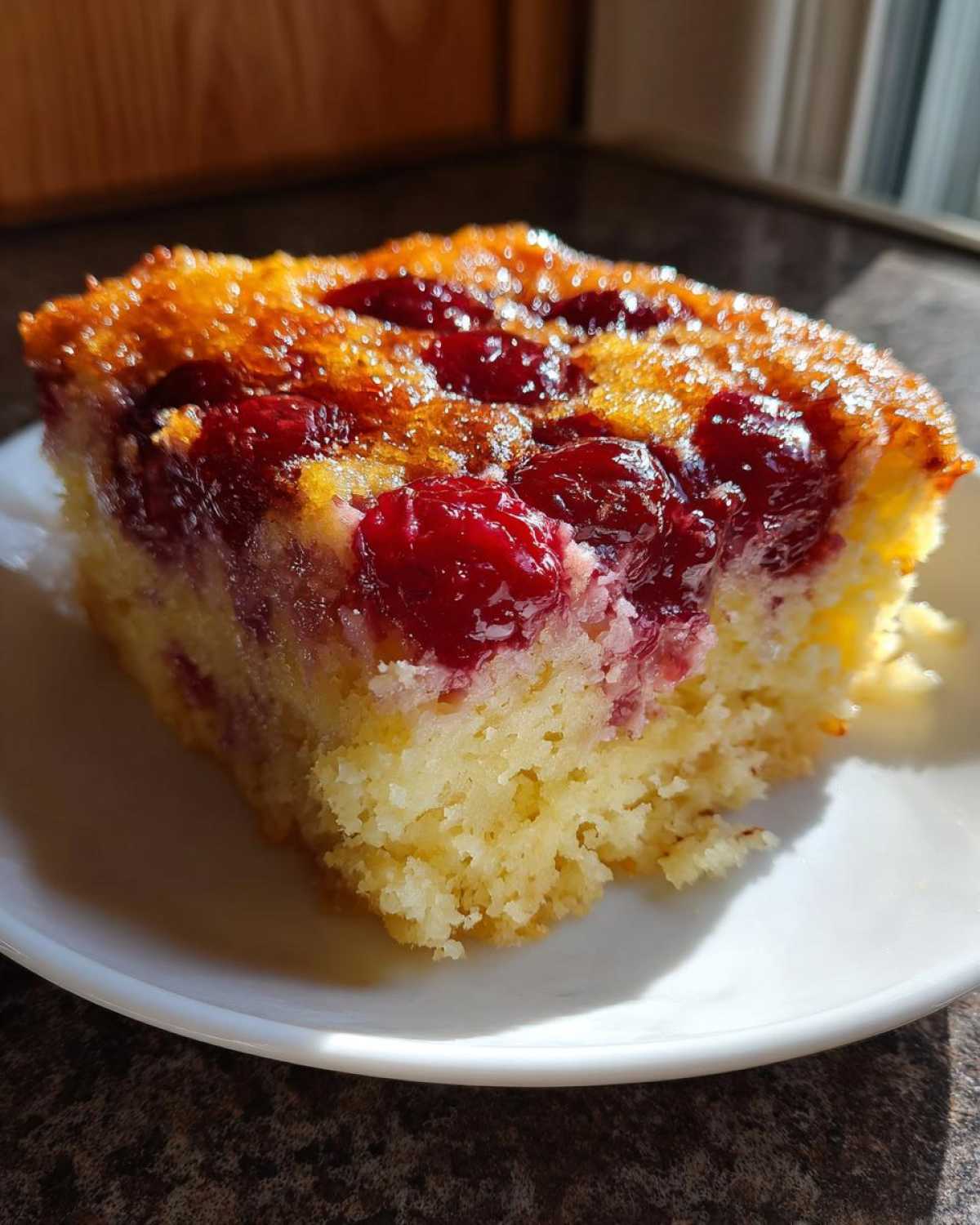 A close-up of a moist slice of cherry dump cake with a golden, caramelized top and bright red cherries.