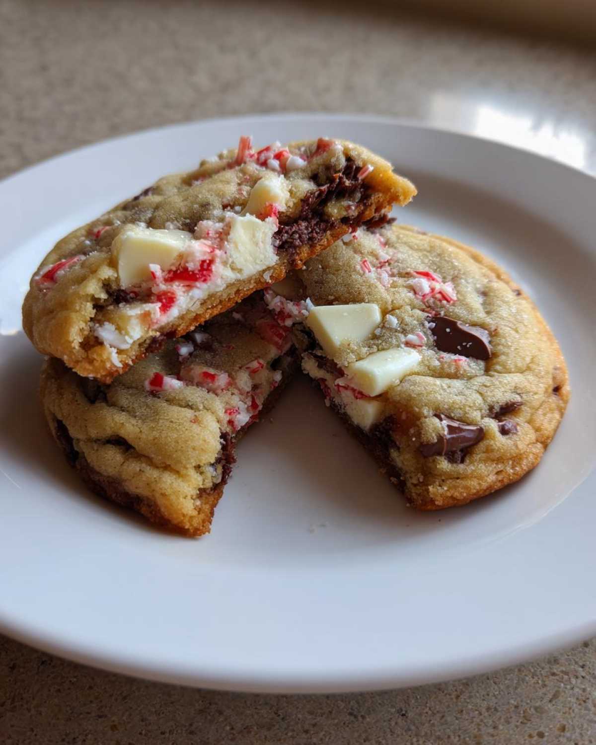 Two halves of a chewy peppermint chocolate chip cookie showing melted chocolate and crushed candy canes inside.