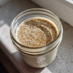 Overhead close-up of creamy chia seed pudding topped with visible chia seeds and cinnamon in a glass mason jar.
