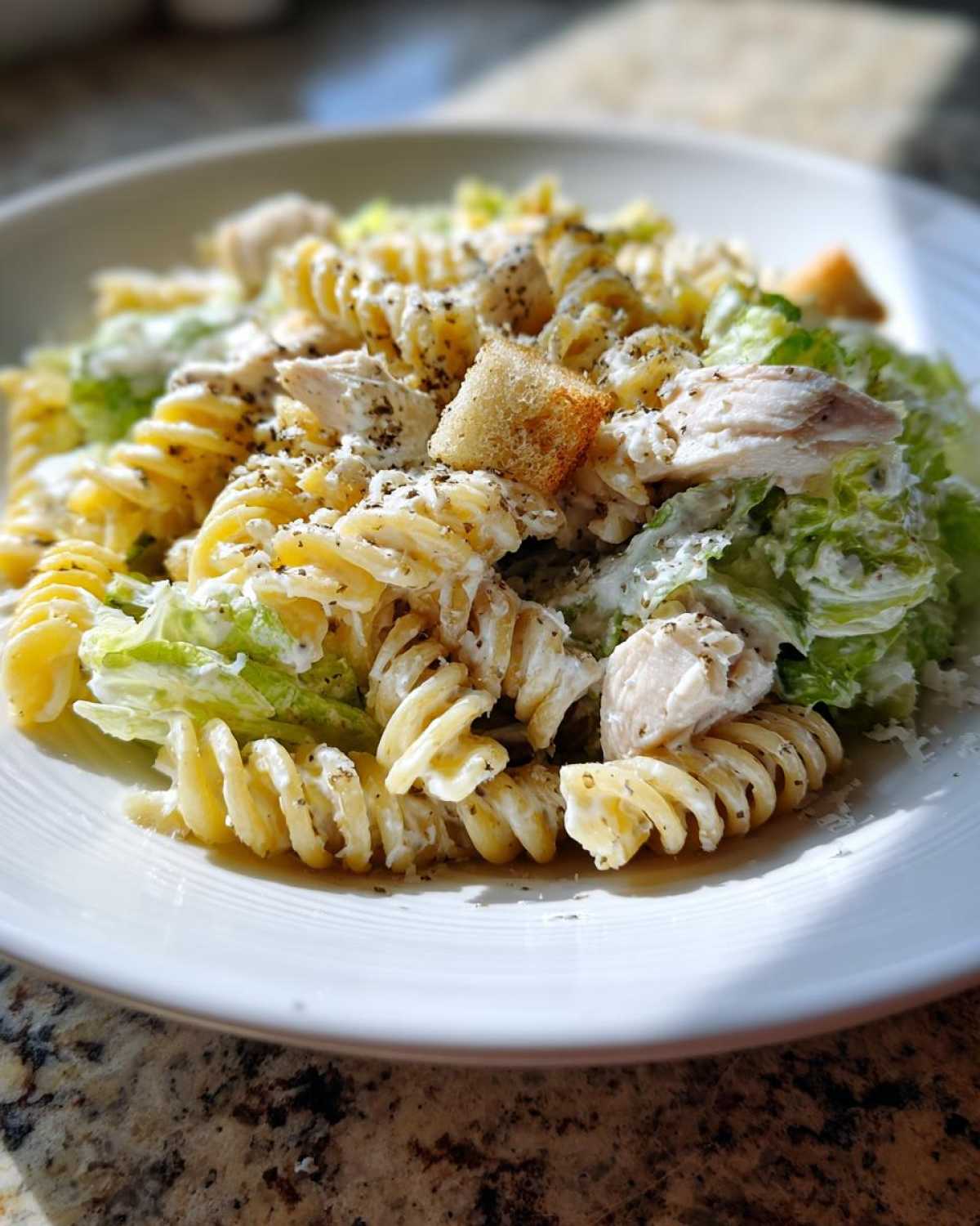 A close-up of a serving of chicken caesar pasta salad featuring fusilli pasta, chicken pieces, romaine lettuce, and creamy dressing.