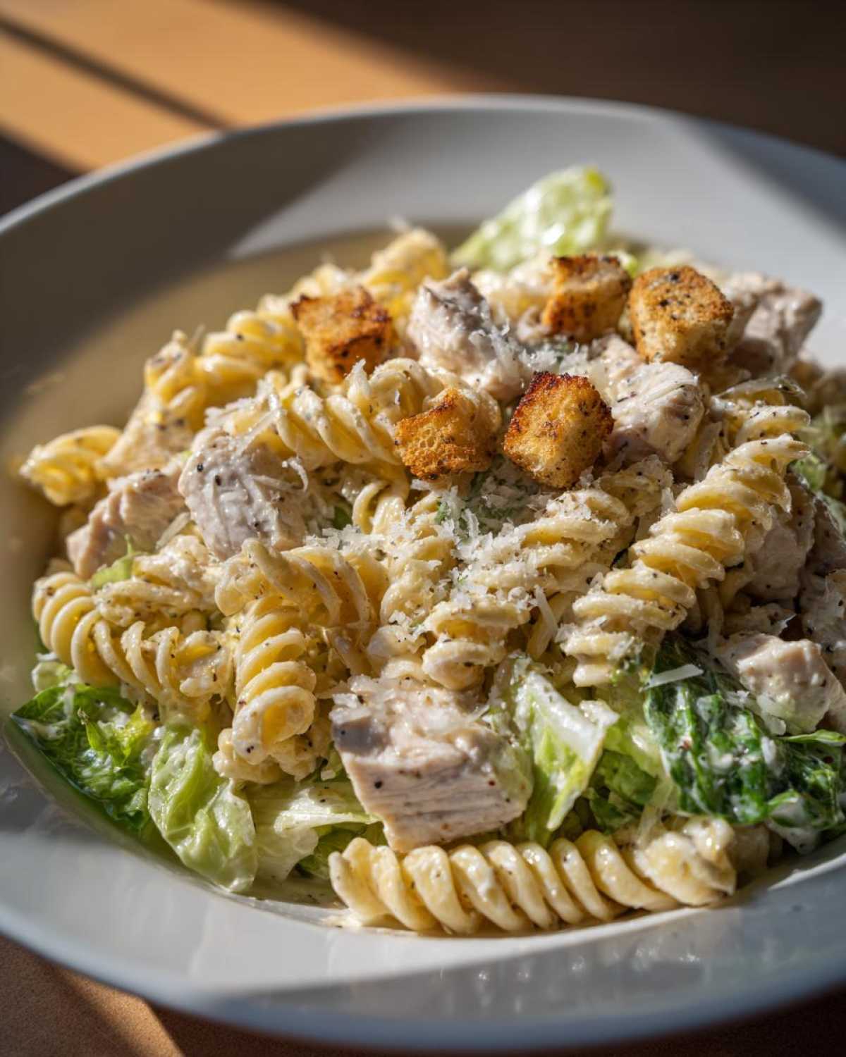 Close-up of a bowl of chicken caesar pasta salad featuring rotini pasta, diced chicken, romaine lettuce, and croutons.