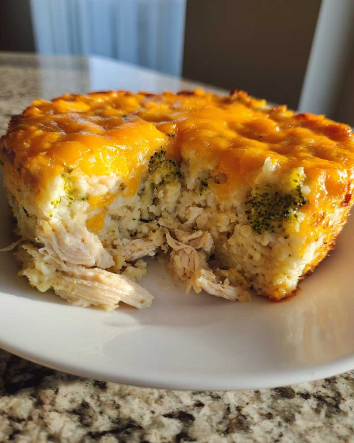 A close-up of a serving of chicken cauliflower rice casserole topped with melted cheddar cheese, showing shredded chicken inside.