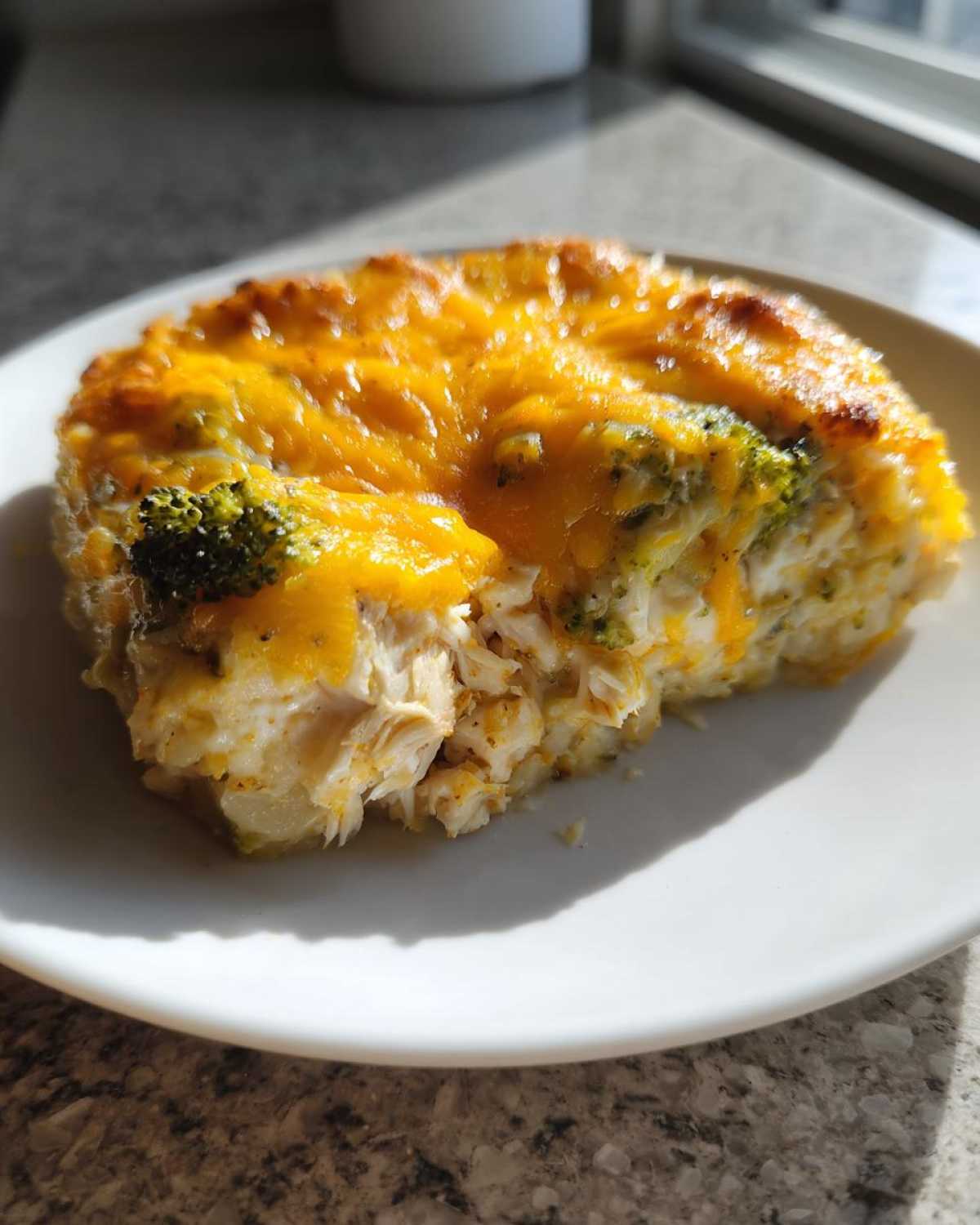 A close-up serving of chicken cauliflower rice casserole topped with melted cheddar cheese and broccoli florets.