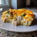 A close-up slice of cheesy chicken cauliflower rice casserole with visible shredded chicken and broccoli florets.