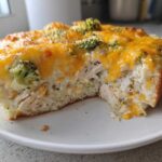 A thick slice of creamy chicken cauliflower rice casserole topped with melted cheddar cheese and broccoli florets.