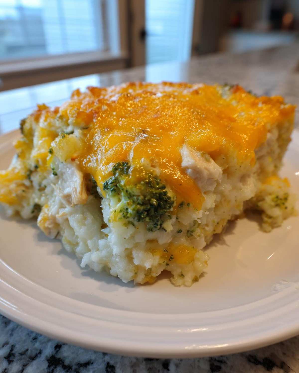 A close-up of a serving of chicken cauliflower rice casserole topped with melted cheddar cheese and broccoli florets.