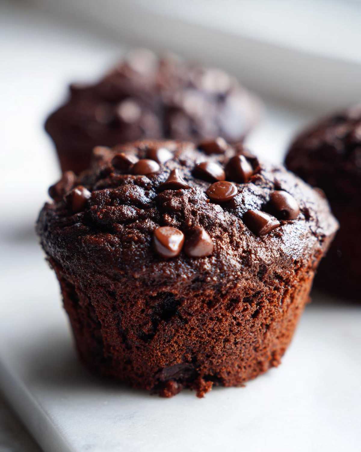 Close-up of a moist, dark chocolate zucchini muffin topped generously with chocolate chips.