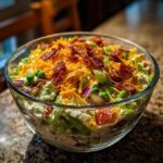 A beautiful, layered glass bowl filled with a classic 7 layer salad topped with bacon and cheese.