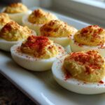 A row of perfectly prepared classic deviled eggs topped with creamy filling and sprinkled with bright red paprika.