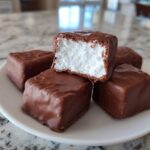 Close-up of several homemade cool whip candy squares coated in chocolate, one piece is cut open showing the white fluffy center.
