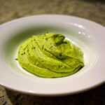 A dollop of vibrant, creamy avocado sauce garnished with flecks of green herbs, served in a white bowl.