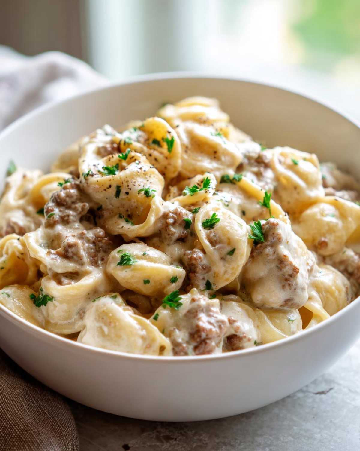 Close-up of creamy beef pasta featuring tortellini or similar shaped pasta coated in a rich white sauce with ground beef, garnished with parsley.