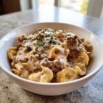 A close-up of a white bowl filled with creamy beef pasta, topped with fresh parsley.