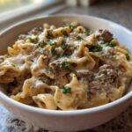 Close-up of a white bowl filled with creamy beef pasta, featuring ruffled noodles and ground beef in a rich sauce, topped with fresh parsley.