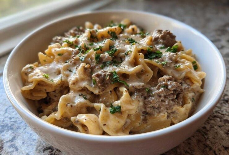 Close-up of a white bowl filled with creamy beef pasta, featuring ruffled noodles and ground beef in a rich sauce, topped with fresh parsley.