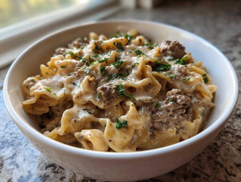 Close-up of a white bowl filled with creamy beef pasta, featuring ruffled noodles and ground beef in a rich sauce, topped with fresh parsley.