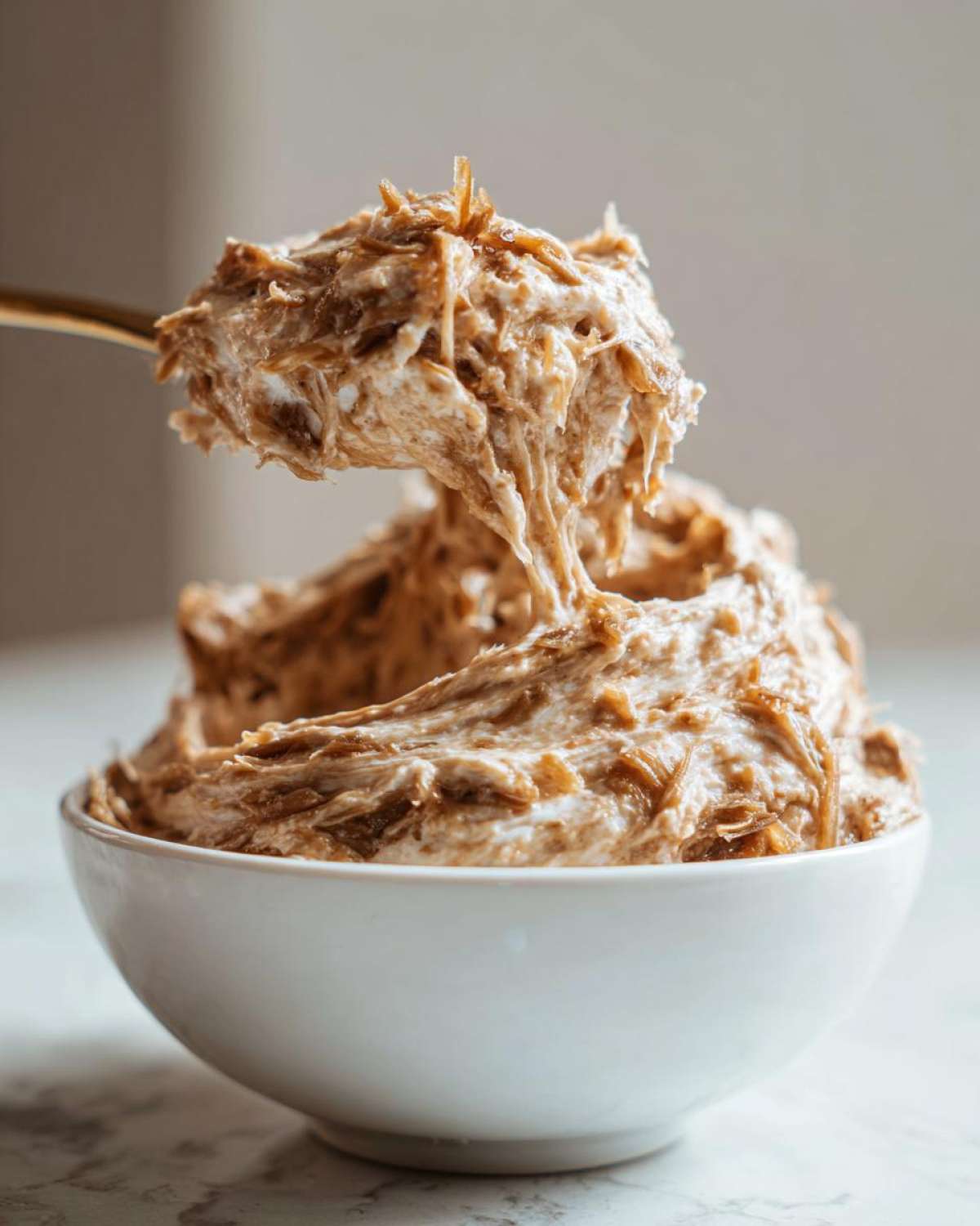 A spoonful of rich, creamy caramelized onion dip being lifted from a white bowl, showing stringy caramelized onions.