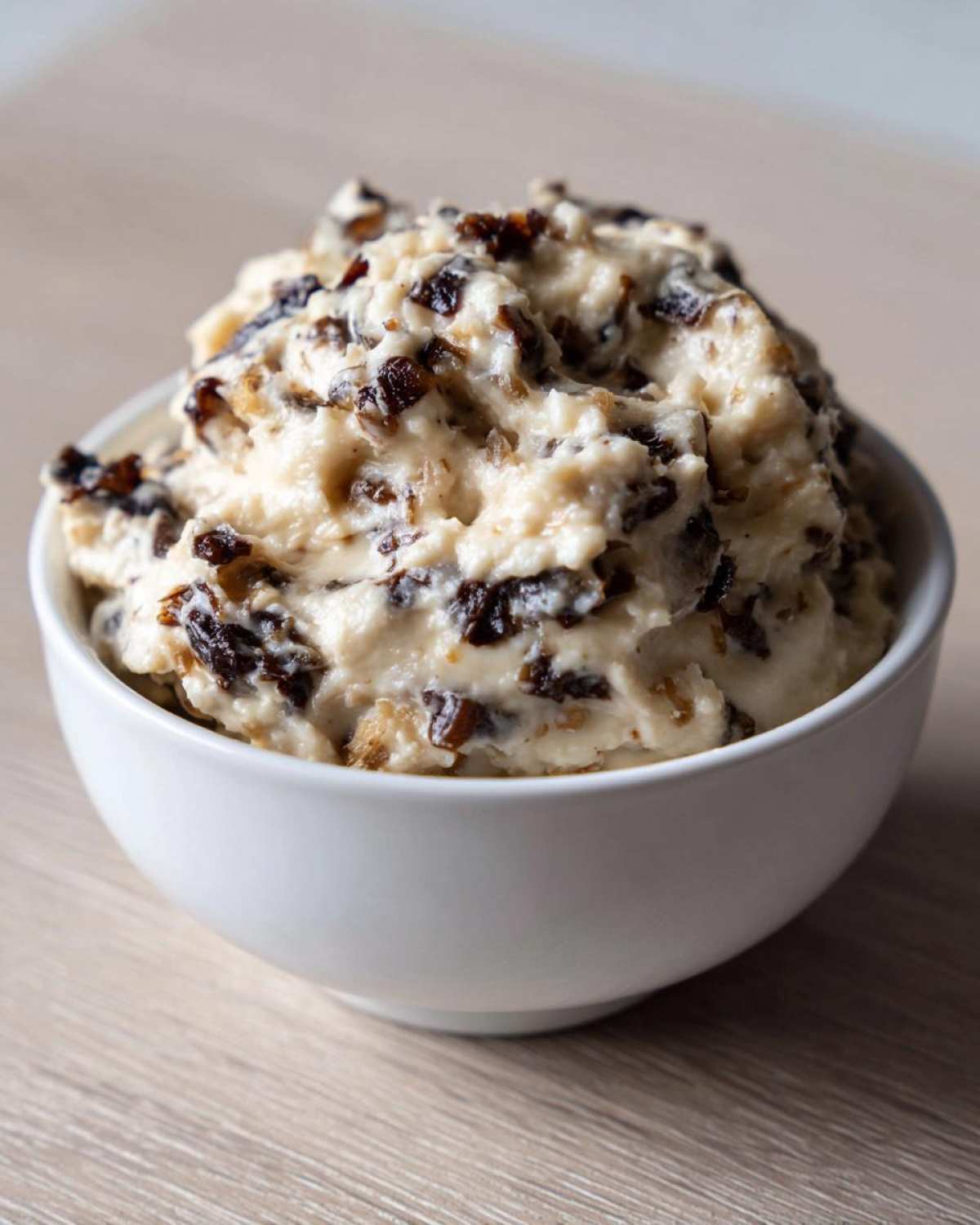 Close-up of a thick, creamy onion dip loaded with dark caramelized onions served in a white bowl.