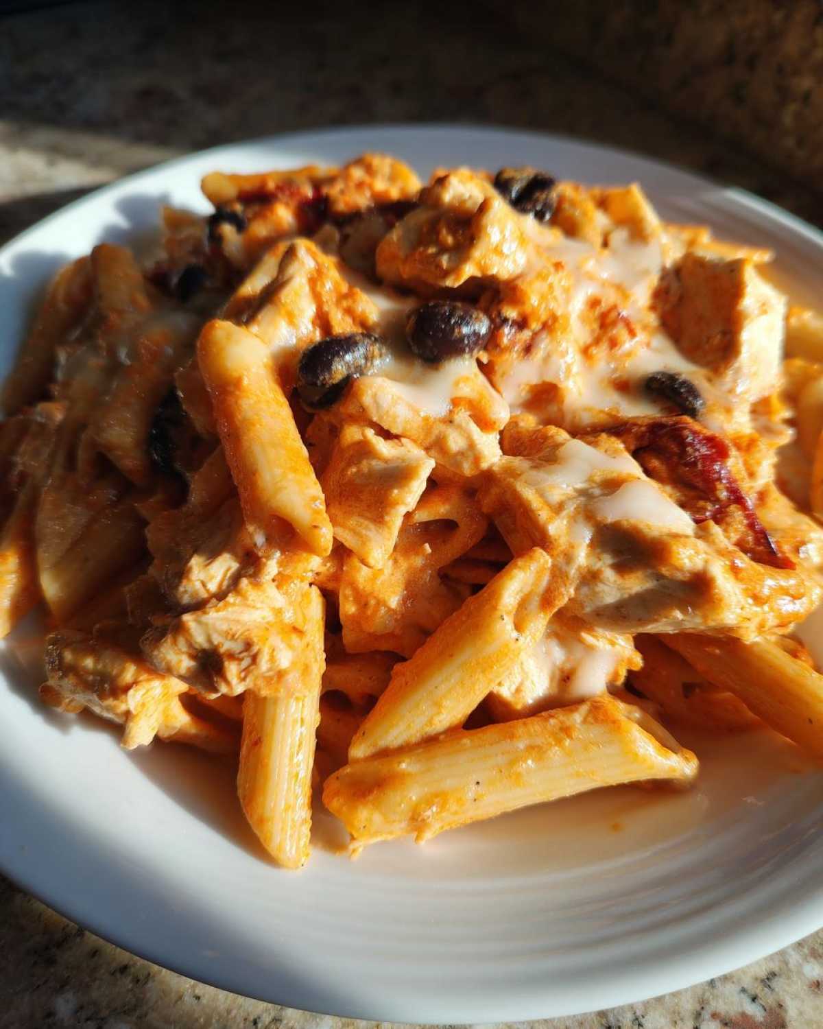 Close-up of creamy chicken enchilada pasta made with penne, chicken chunks, olives, and melted cheese.