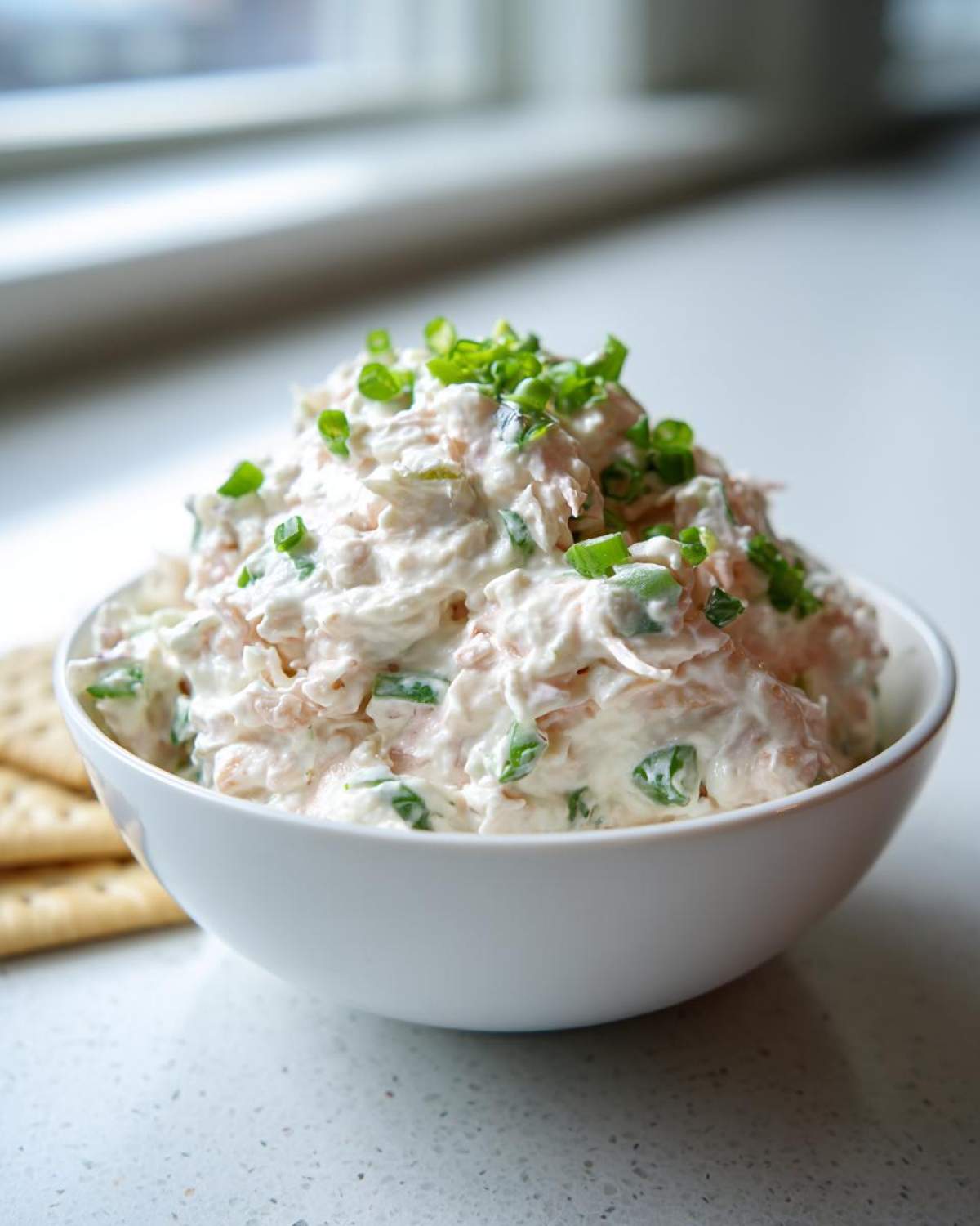 A white bowl filled with creamy clam dip, garnished generously with chopped green onions.