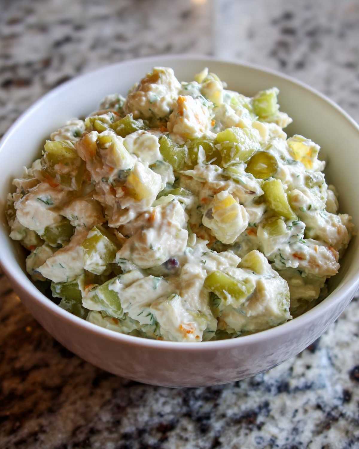 Close-up of a white bowl filled with creamy dill pickle chicken salad featuring chunks of chicken and bright green pickles.