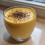 Close-up of a glass filled with creamy yellow eggnog, topped with freshly grated nutmeg.