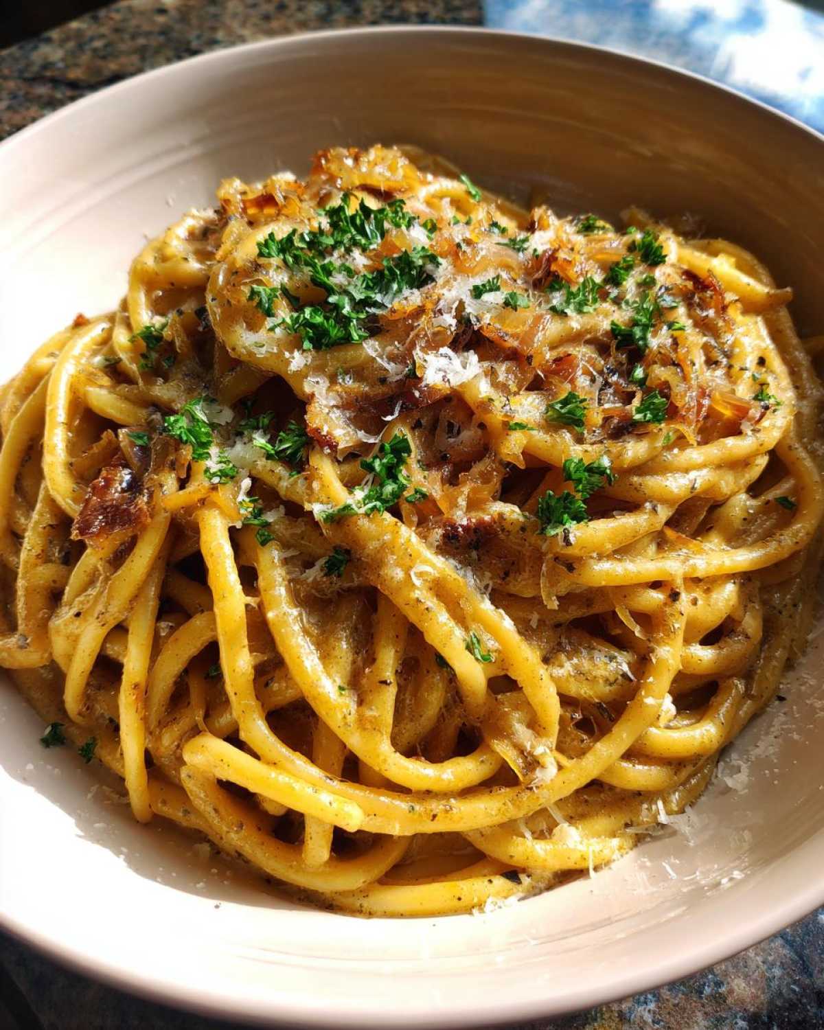 Close-up of a bowl of creamy french onion pasta, garnished with caramelized onions, grated cheese, and fresh parsley.