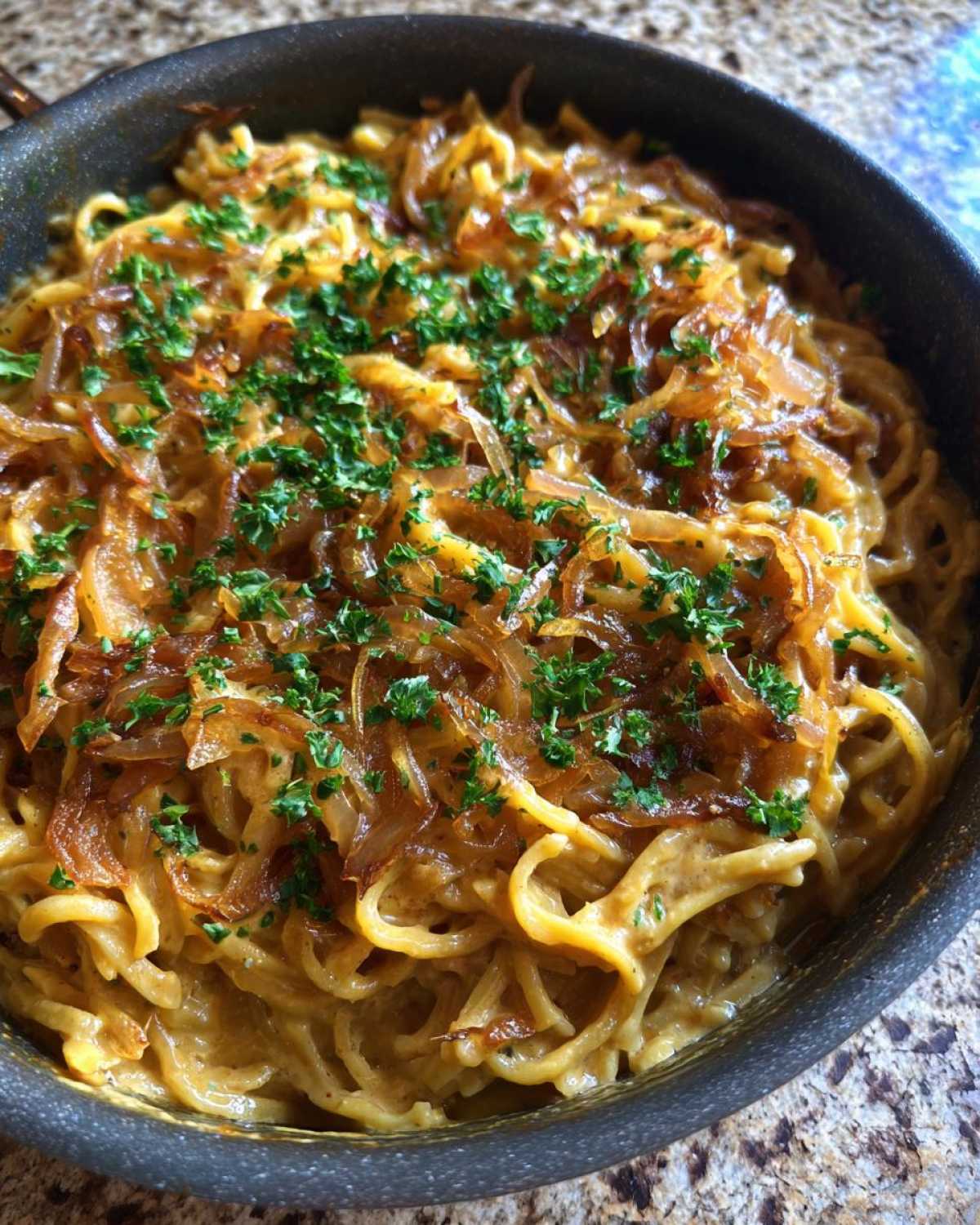 A close-up of creamy french onion pasta in a skillet, generously topped with caramelized onions and fresh parsley.