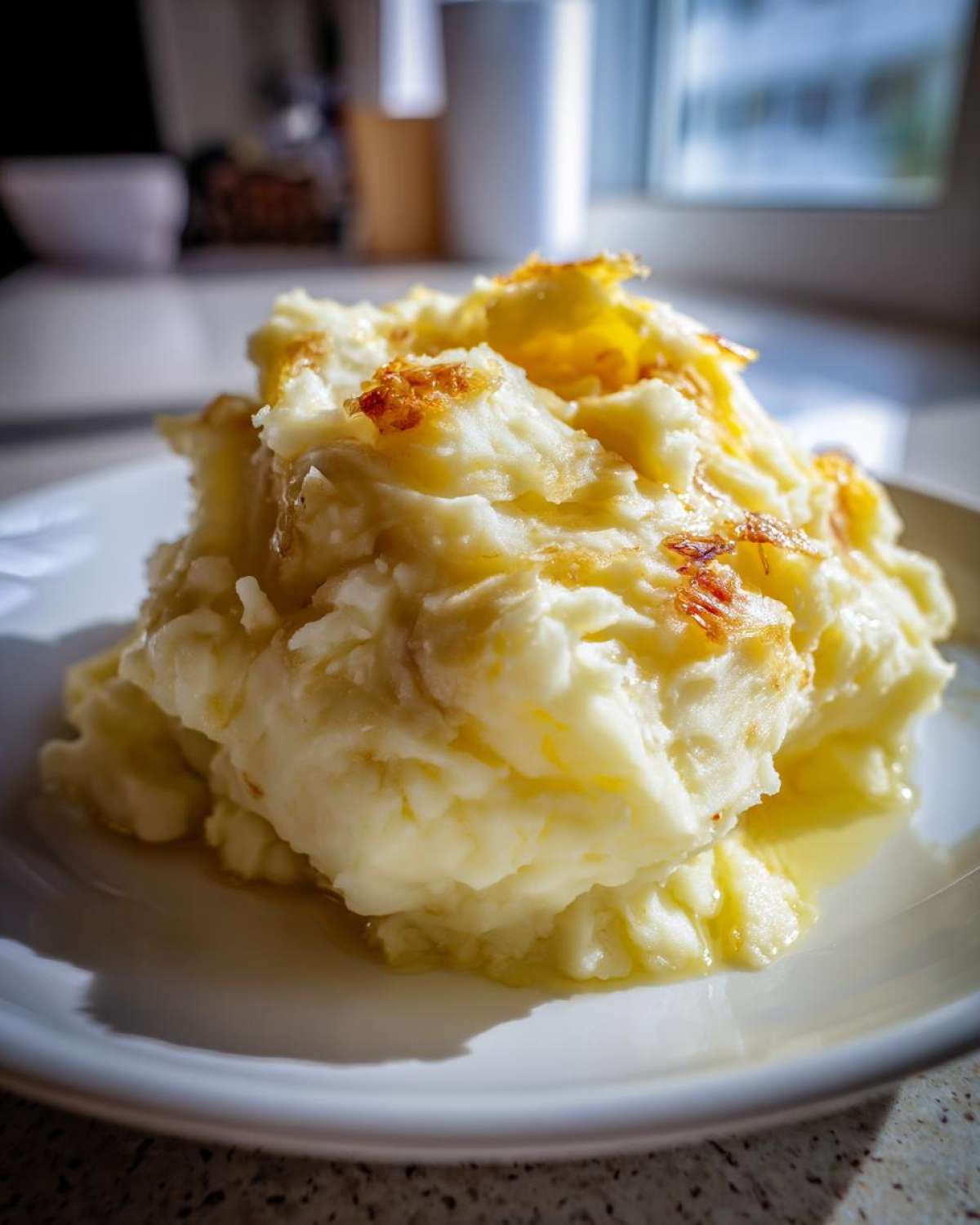A generous serving of creamy garlic mashed potatoes topped with crispy browned bits on a white plate.
