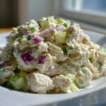 Close-up of creamy greek yogurt chicken salad mixed with chunks of celery and red onion on a white plate.