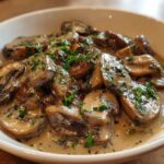 Close-up of rich, creamy mushroom sauce generously covering sliced mushrooms, garnished with fresh parsley.