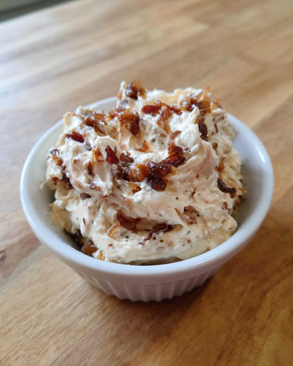 Close-up of creamy onion dip in a white ramekin, topped generously with caramelized onions.