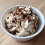 A white bowl filled with creamy onion dip, generously topped with dark, caramelized onions.