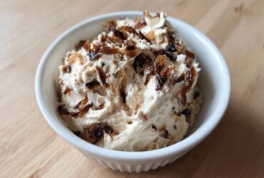 A white bowl filled with creamy onion dip, generously topped with dark, caramelized onions.