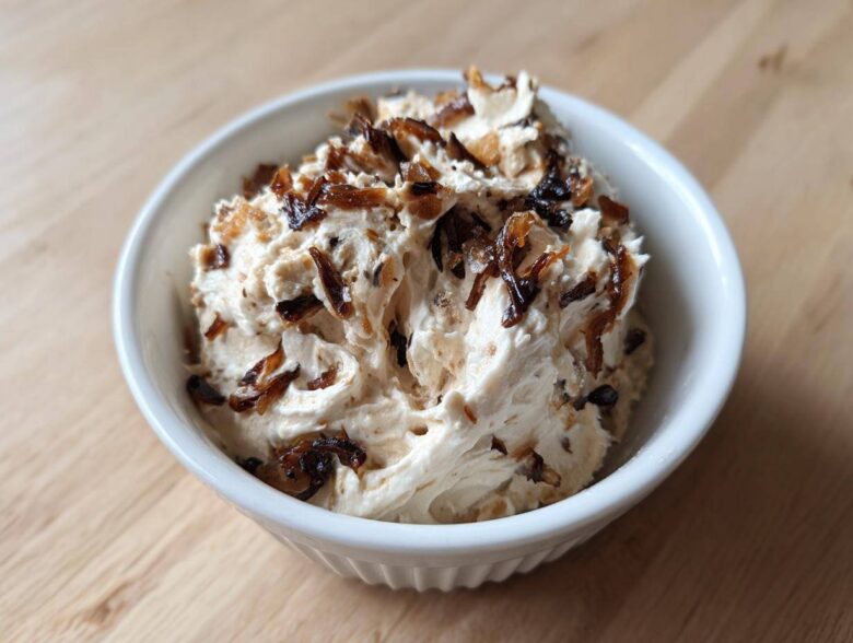A white bowl filled with creamy onion dip, generously topped with dark, caramelized onions.