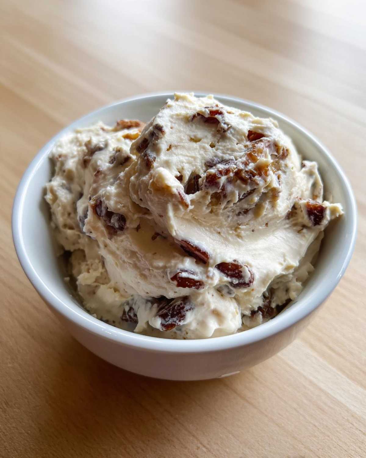 Close-up of creamy onion dip mixed with dark, caramelized pieces served in a small white bowl.