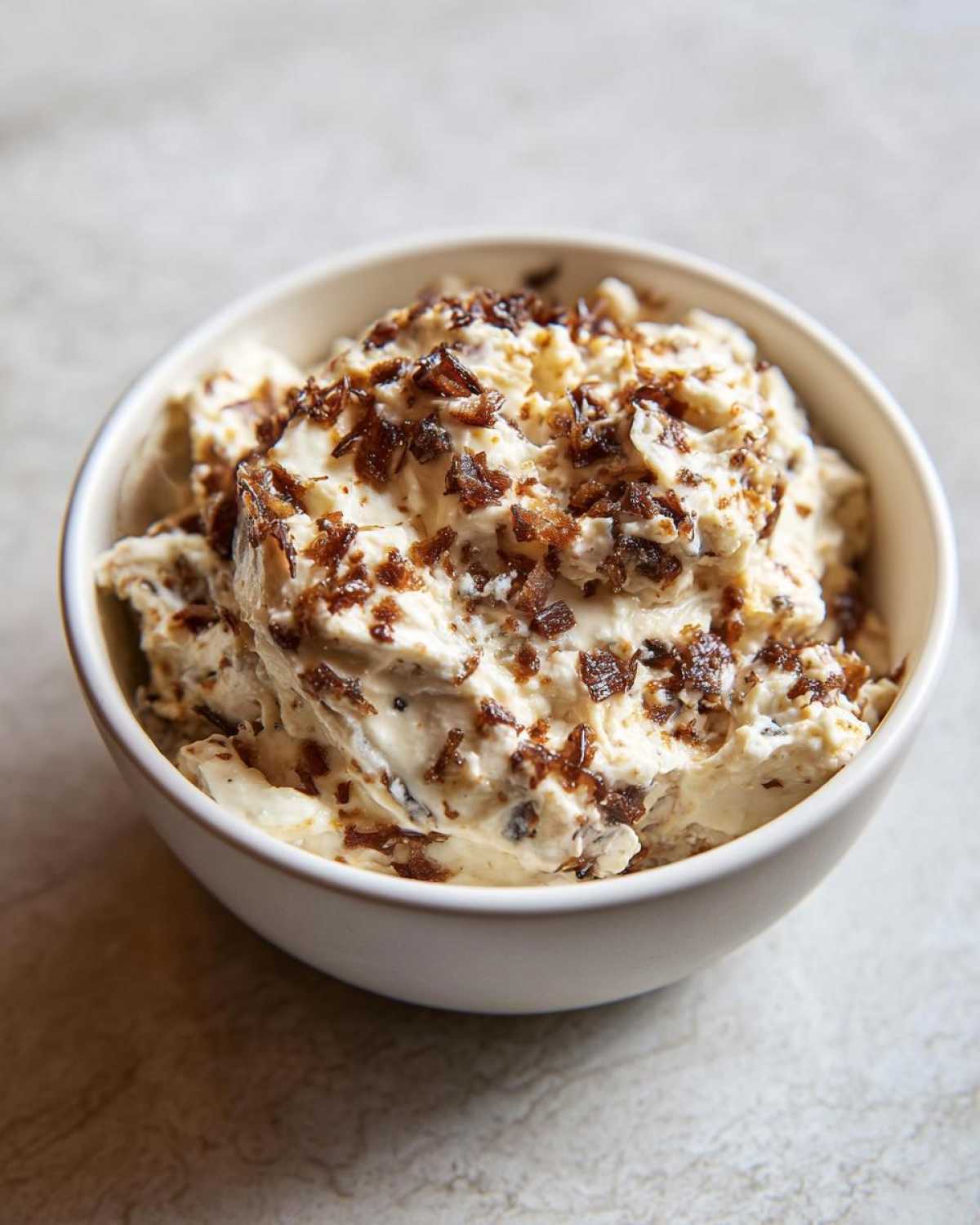 Close-up of a white bowl filled with creamy onion dip topped generously with crispy, browned onion pieces.