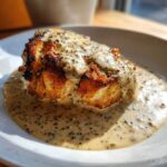A piece of seared meat generously covered in creamy peppercorn sauce served in a white bowl.