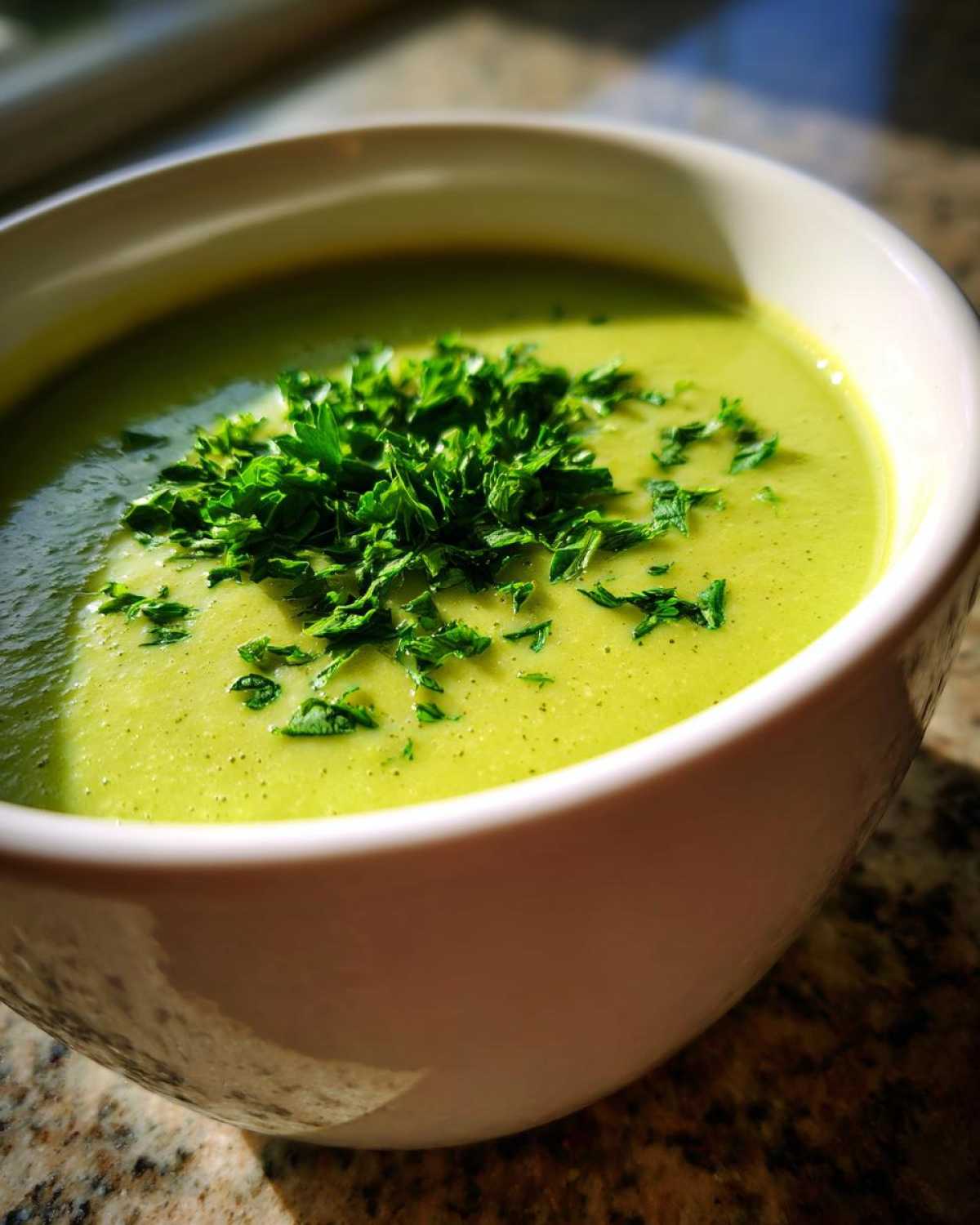 Close-up of a bowl of bright green zucchini soup topped generously with chopped fresh parsley.