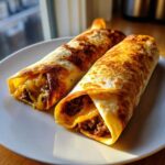 Two golden-brown, crispy chimichangas filled with seasoned ground beef and melted cheddar cheese on a white plate.