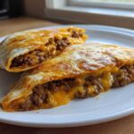 Two halves of a crispy, golden-brown chimichanga, cut open to show the seasoned ground beef and melted cheddar cheese filling.