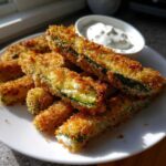 A plate of golden brown, crispy fried pickles served with a side of creamy white dipping sauce.