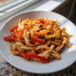 Shredded chicken mixed with colorful sliced bell peppers and onions, ready for crockpot chicken fajitas.
