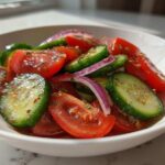 Close-up of a vibrant cucumber tomato salad with red onion slices, dressed and seasoned.