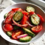 Close-up of a vibrant cucumber tomato salad with red onion slices, heavily seasoned.